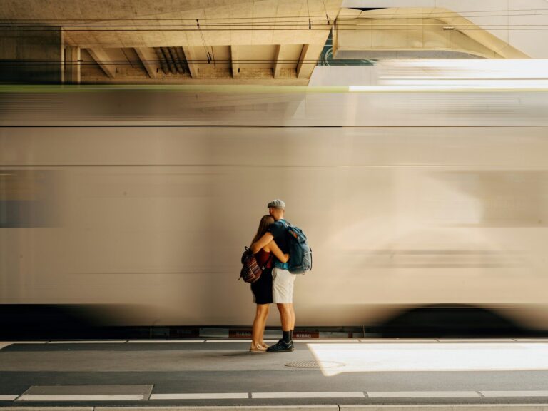 Two people with backpacks hugging on a train platform as a train passes